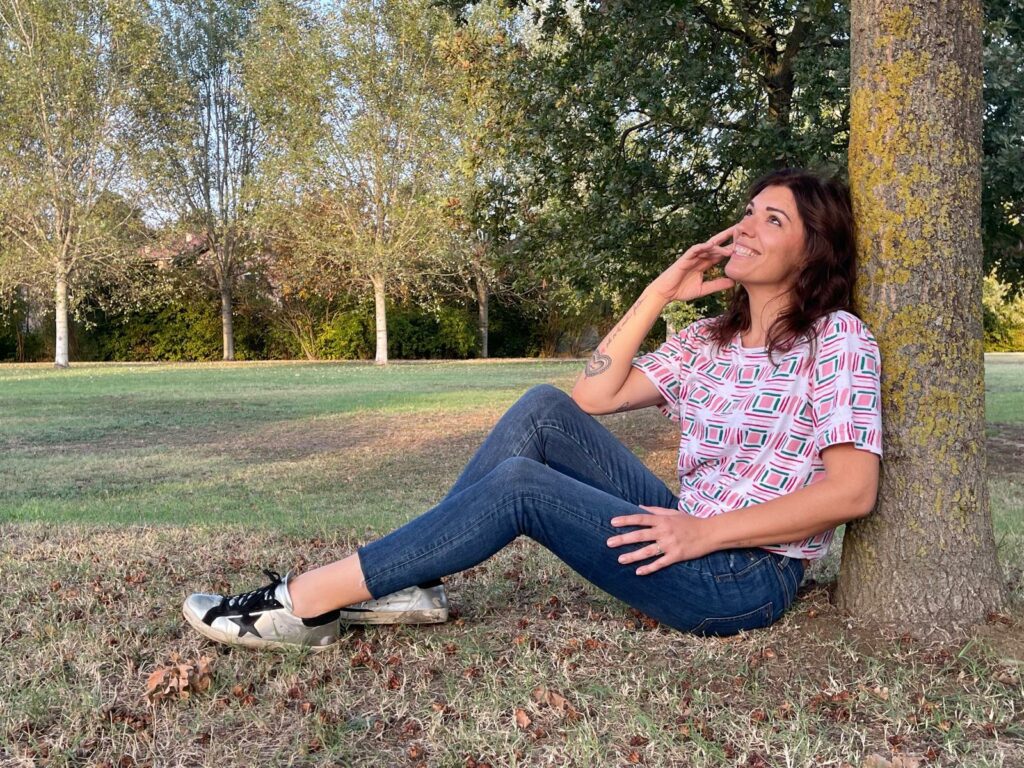 Francesca Berti seduta contro un albero in un parco, sorridente e serena durante una sessione di meditazione all'aperto.